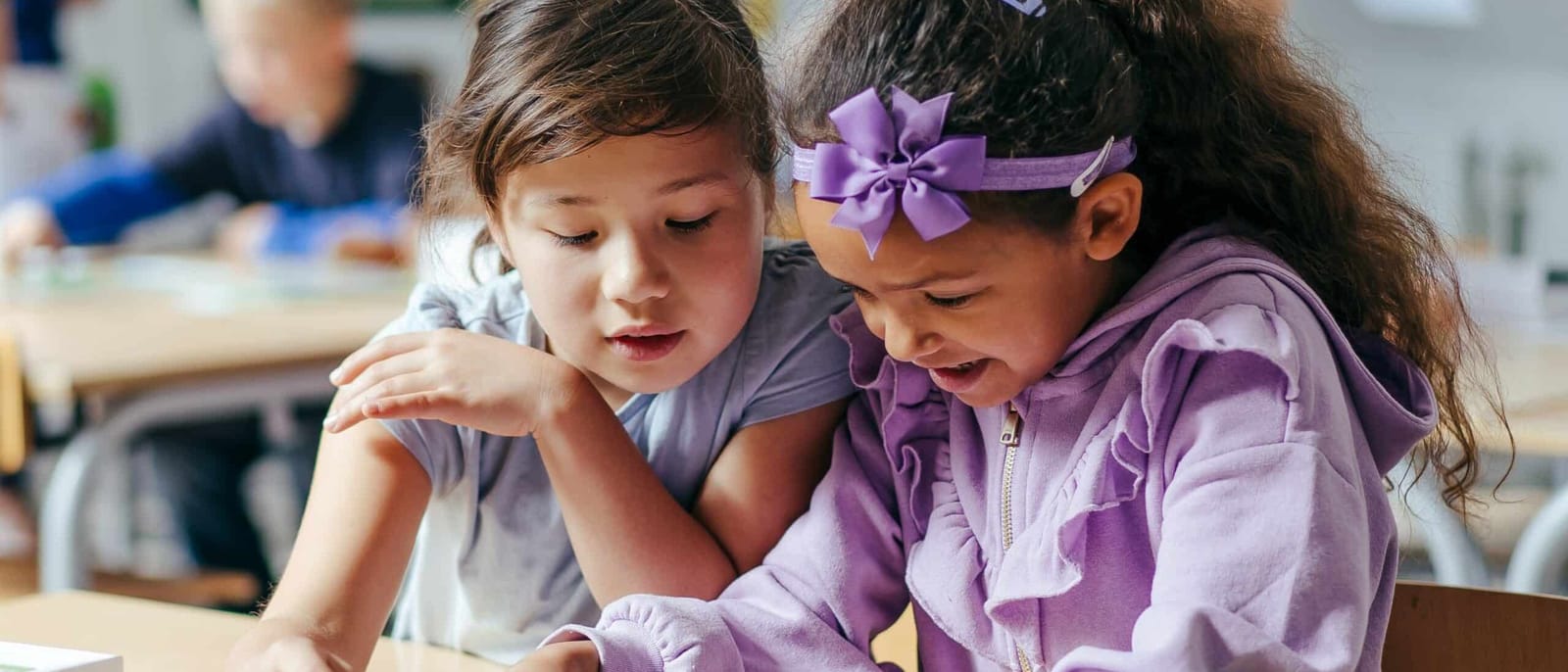 Two students leaning in together over a KUBO activity map in a classroom